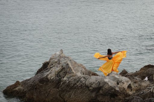 A woman wearing a yellow dress dancing on the stone near the sea