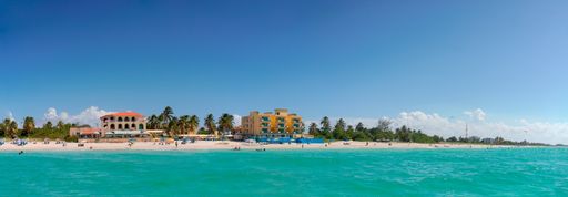 A panoramic shot of the sea surrounded by the beach and greenery under the sunlight