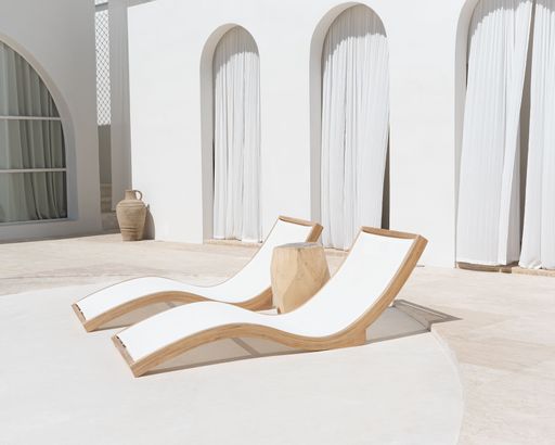 Two beautiful simplistic curved beach chairs near a stone wall with arches and curtains