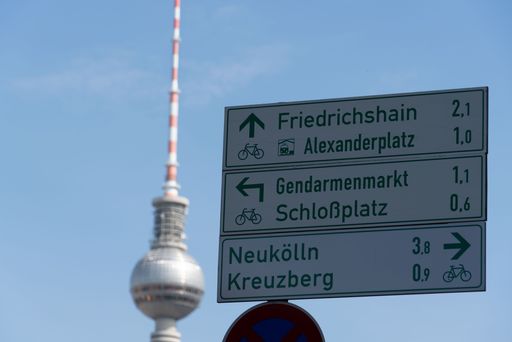 A closeup shot of a street sign showing directions to Alexanderplatz, Schlobplaz, and Kreuxberg on a blue sky background