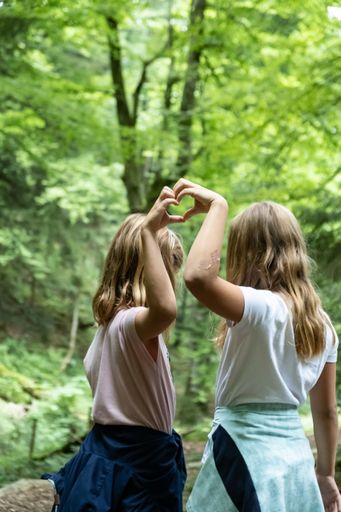 A back view of two Caucasian ladies doing a heart sign with their hands