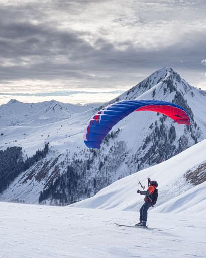A back view of human with parachute standing snow covered field in background of mountains