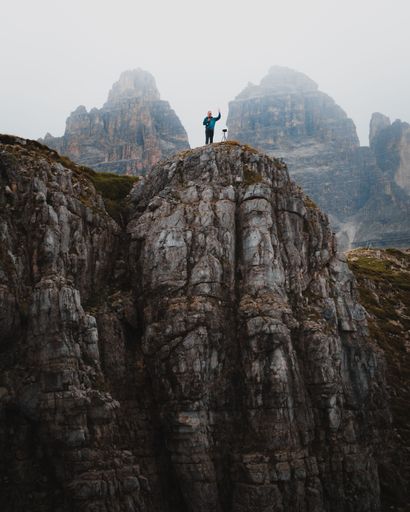 A vertical of a hiker standing on the edge of rugged Dolomites mountains and showing a peace sign