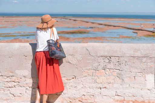A woman with a sun hat on leaning on a stone wall and enjoying the scenic seascape view