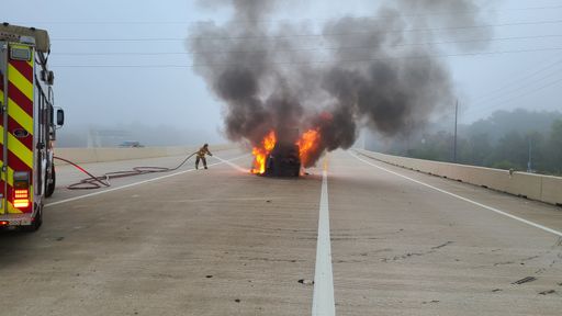 A fireman extinguishing a burning car with black smoke
