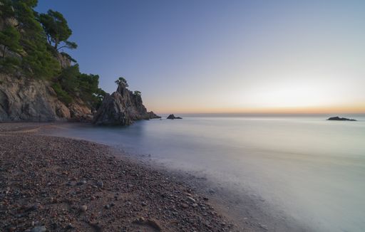An amazing view of the sea and the shore with a cliff full of trees and the beautiful horizon in the background