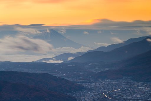 An aerial shot of a town and Mount Fuji in the distance around clouds, golden hour