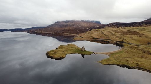 A gorgeous aerial view of the castle in Eilean Donan, Scotland with the misty white clouds reflected in the quiet waters