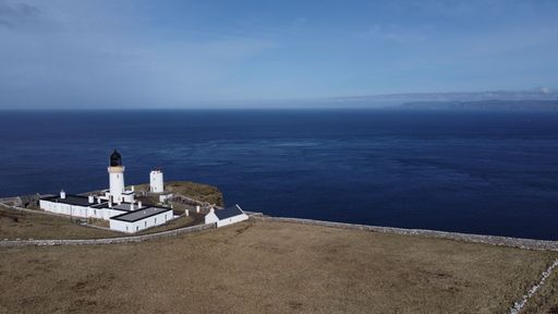 A lighthouse overlooking the calm dark blue sea under a sunny sky in Scotland