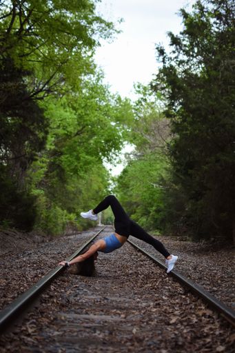 A beautiful young woman in a blue top doing yoga on a railroad track