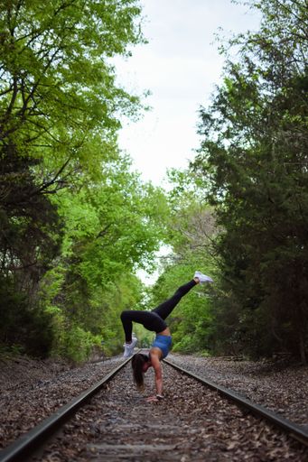 A beautiful young woman in a blue top doing yoga on a railroad track