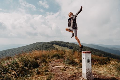 A kid jumping from the stone pillar. Fluffy clouds over countryside in the background. Concept of freedom