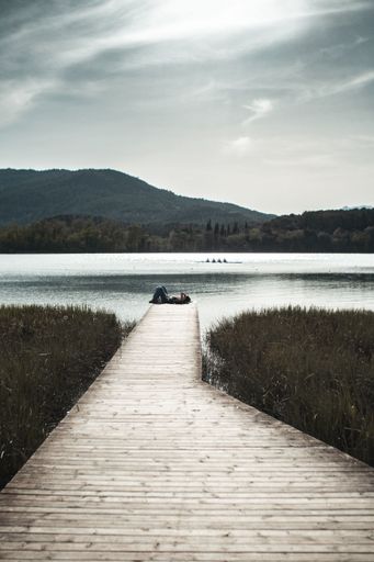 A vertical shot of a girl laying on the wooden pier against a lake on a sunny day