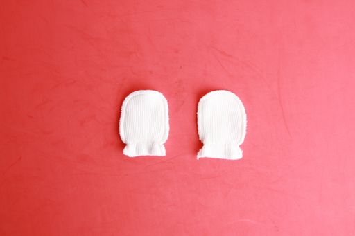 A top view of white wool baby mittens on a red background