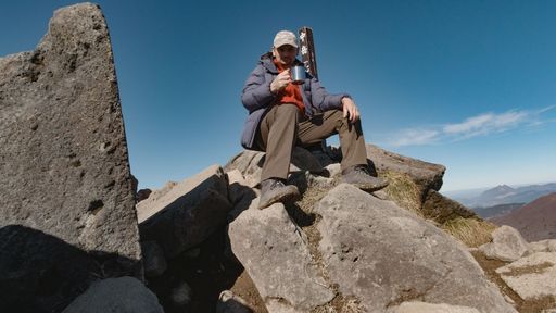 A man resting atop bick rocks, enjoy a cup of hot coffee on his break from hiking in Kuju, Japan