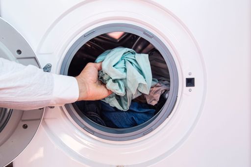 A closeup of a hand of a man putting dirty cloth into the washing machine
