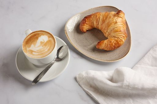 A French croissant with coffee and small spoon on marble surface