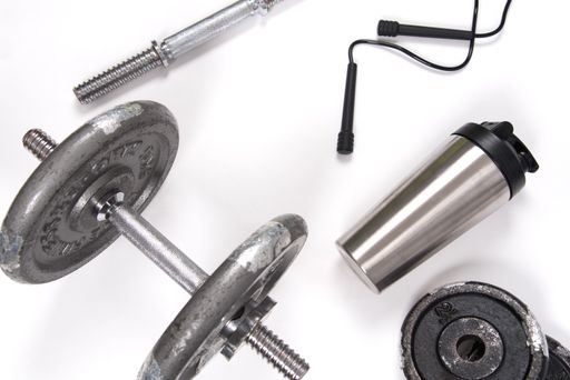 A high angle shot of dumbbells with exercising ropes and a water bottle on a white yoga mat