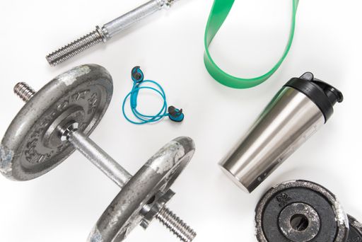 A high angle shot of dumbbells with exercising ropes and a water bottle on a white yoga mat