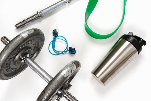 A high angle shot of dumbbells with exercising ropes and a water bottle on a white yoga mat