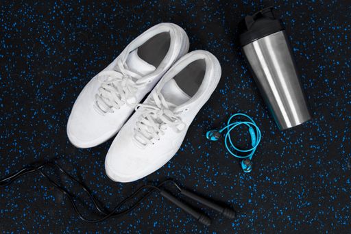 A top view of a pair of white trainers with a water bottle and headphones on the floor