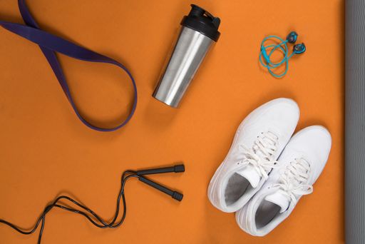 A top view of a pair of white trainers with a water bottle on a yoga mat with exercising ropes on it