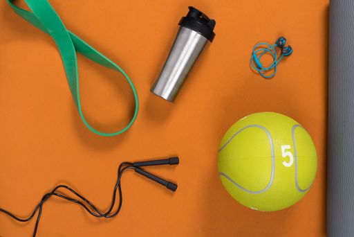 A top view of a water bottle and a ball on a yoga mat with exercising ropes and headphones on it