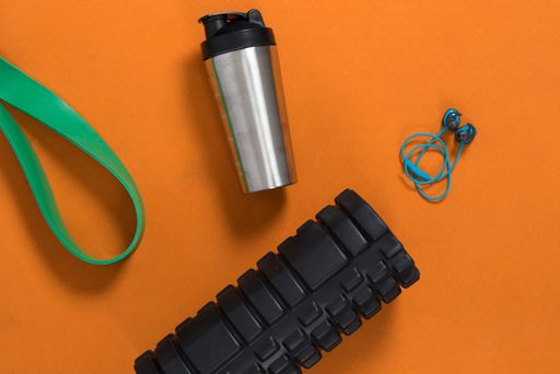 A top view of a water bottle on a yoga mat with exercising ropes and headphones on it