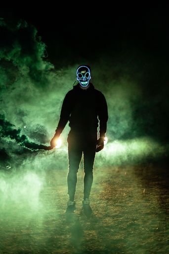 A vertical shot of a masked man holding a green smoke bomb.