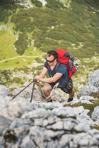 A high-angle view of a young male hiker with a backpack climbing up the rocks