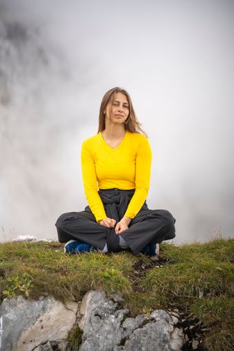 A vertical shot of a young girl sitting on the top of a mountain against white fog