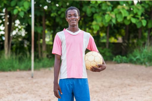 A closeup shot of an African boy holding a ball on a sunny day