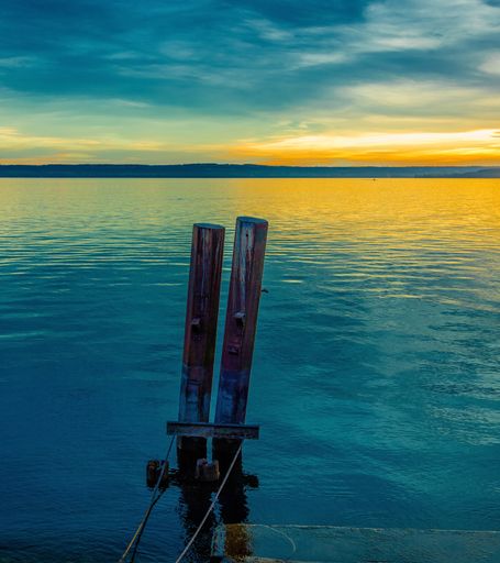 Two logs of wood in the middle of a sea with the reflection of the sunrise in the water