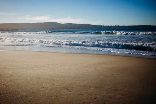 A lovely view of calm blue waves washing up on the smooth bronze-brown sand at a beach in San Francisco