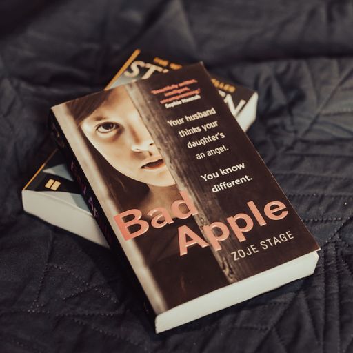 A closeup of Zoje Stage's Bad Apple novel laying on a dark gray bed sheet