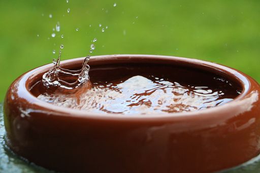 A closeup shot of falling raindrops in a ceramics barrel full of water