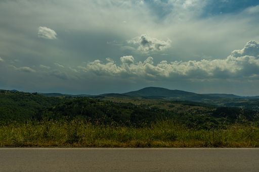 The beautiful grass covered field by a highway with the hills in the background under the clouds