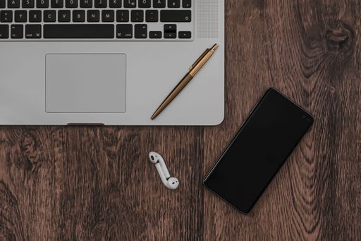 A top view of earphones near a smartphone and a pen on a laptop on the wooden table in Koper, Slovenia