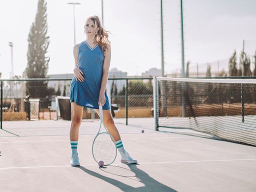 A female tennis player on a court standing near net with racket in her hand