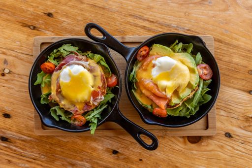 A top view of Egg Benedicts, breakfasts with egg and bacon served in pans on a wooden board