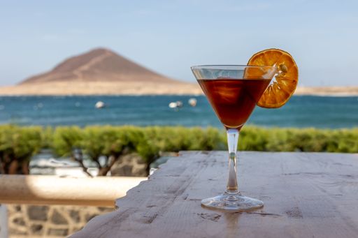 A blood and sand cocktail, mixed drink in a glass decorated with a lemon slice against a beach view