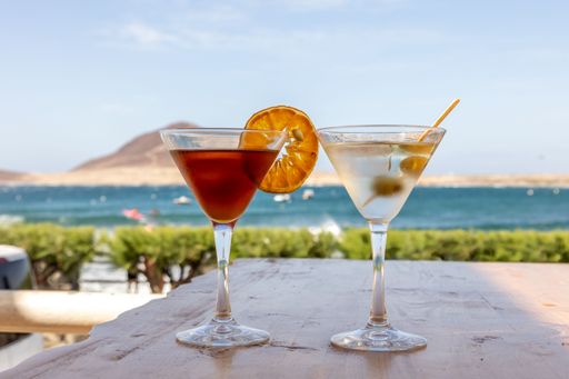 A closeup of two glasses of cocktails on a table with a beautiful sea in the background