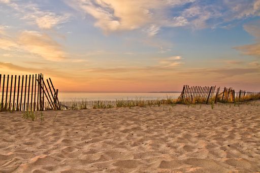 A beautiful sunset sky over the sea and sandy beach, with a wooden fence in the background