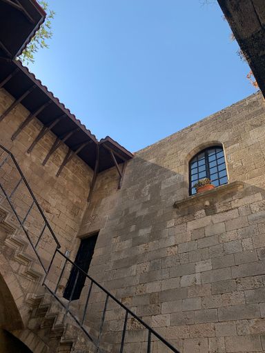 A vertical low angle shot of medieval stone building with outdoor stairways in Rhodes Old Town, Greece