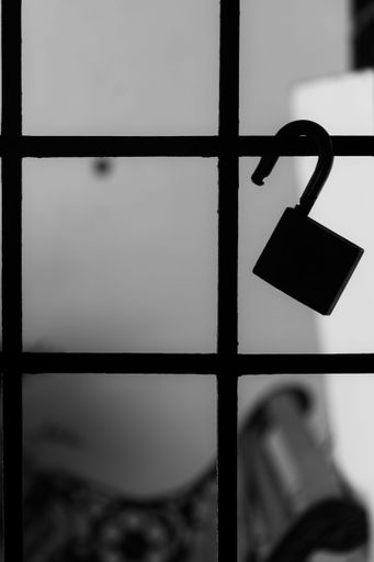 A greyscale shot of an unlocked padlock hanging on a rusty gate