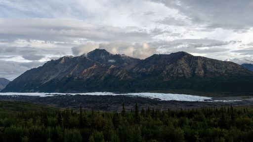 A distant shot of a high mountain range with rocky peaks under the clouded sky