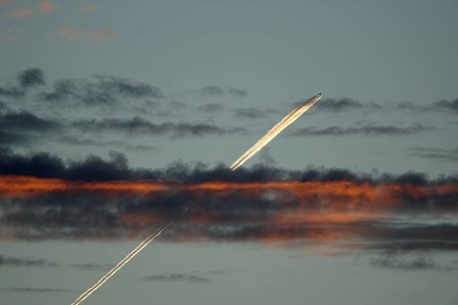 A jet soaring through smoky black and red clouds, leaving a glowing trail behind it in a dark sky