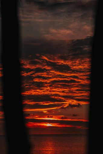 A vertical view of a sunset with the sky a vibrant shade of red reflected in the ocean