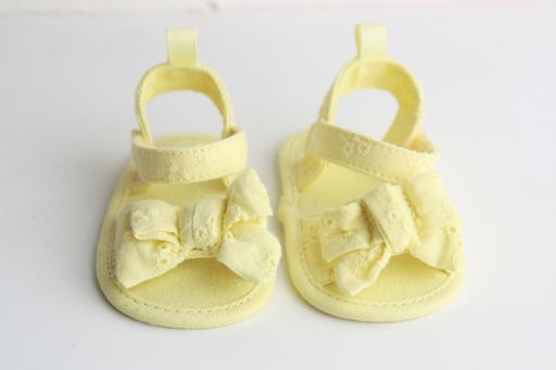 A selective focus closeup shot of a pair of yellow baby sandals with bow design on a white background