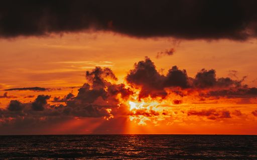 A view of a sunset with the sky a vibrant shade of red reflected in the ocean
